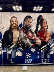 A graphic of Sami Zayn, "The Original Tribal Chief" Roman Reigns, and "The EST of the WWE" Bianca Belair.